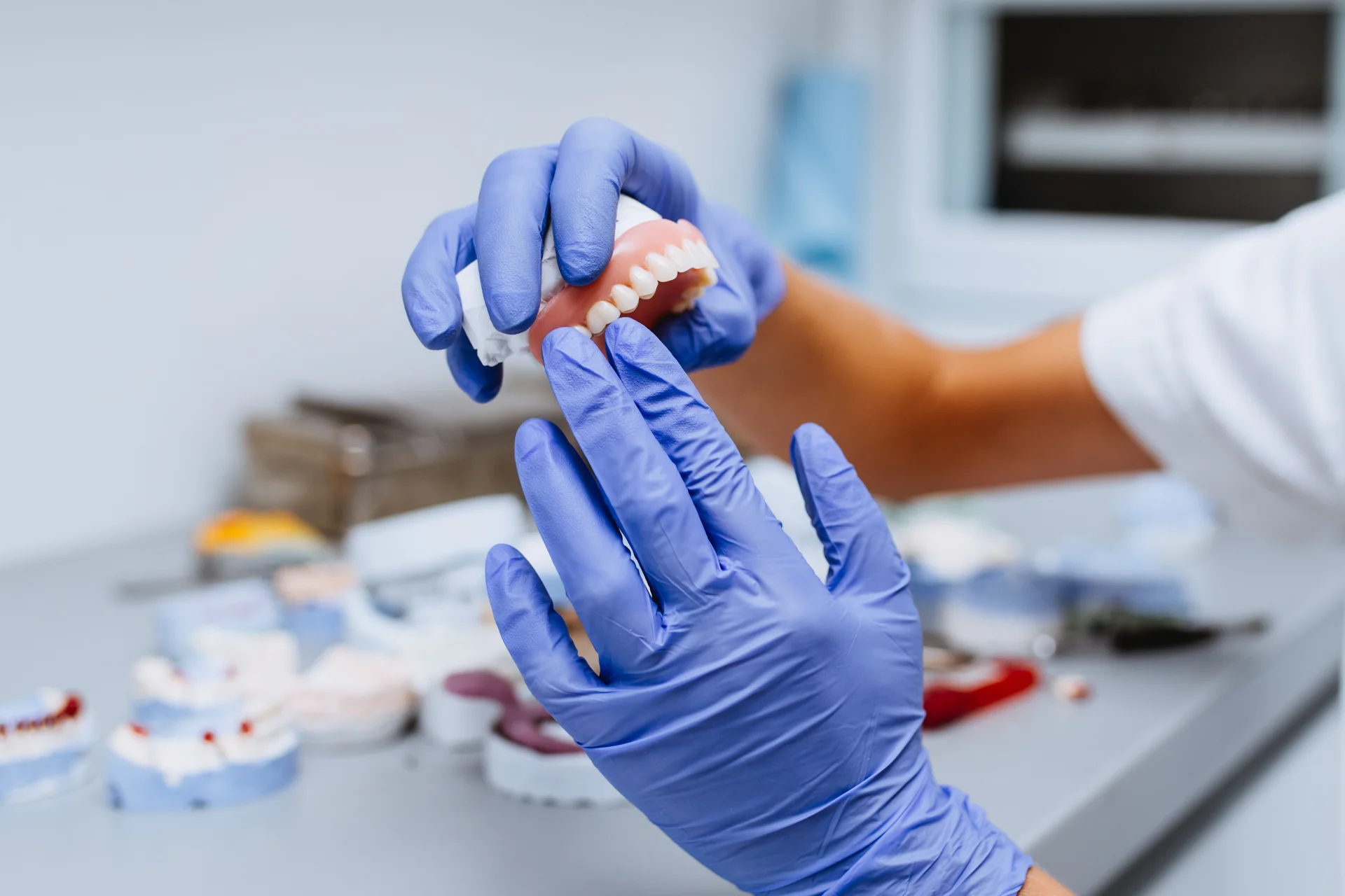 Clinician in blue gloves holding a full upper denture
