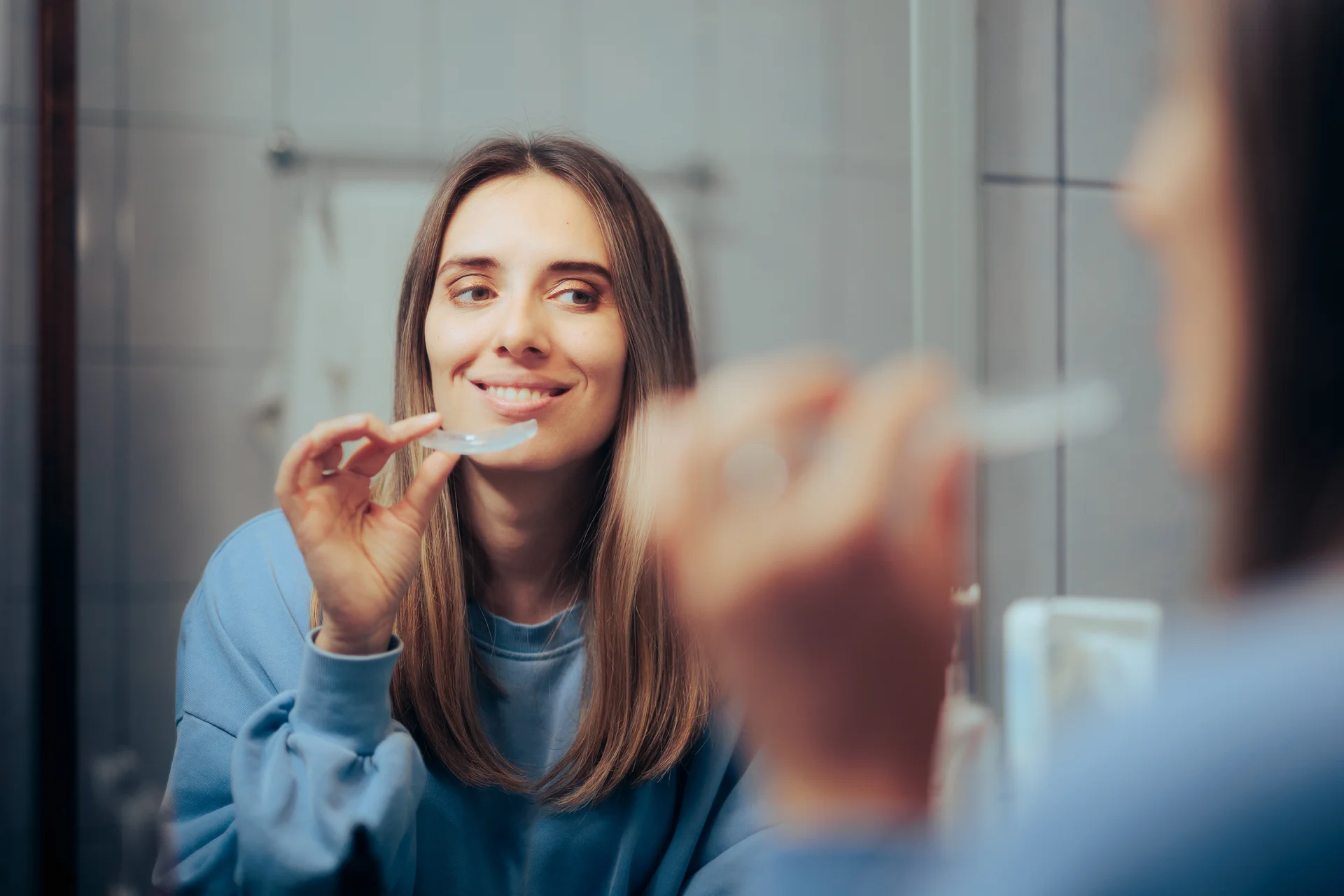 Woman smiling while holding a clear night guard in front of a mirror
